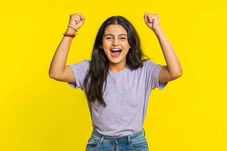 Happy joyful Indian woman celebrating success victory, winning birthday, lottery jackpot goal achievement play game good positive news, triumph. Young Arabian girl isolated on yellow studio backgroundの写真素材