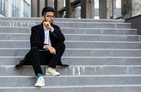 Unhappy sad Indian business man frustrated stress pensive feeling bad after company unemployment lost job problem solution crisis outdoor. Arabian Hindu freelancer guy sitting on stairs downtown cityの写真素材