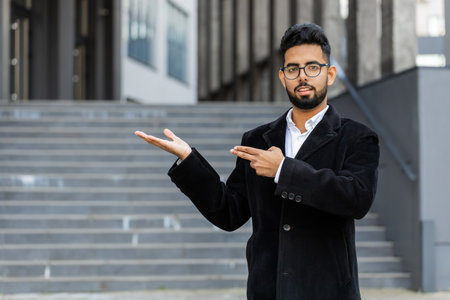 Indian businessman showing pointing empty place advertising area for commercial text copy-space for goods promotion outdoors. Arabian Hindu freelancer guy in downtown city street. Business peopleの写真素材