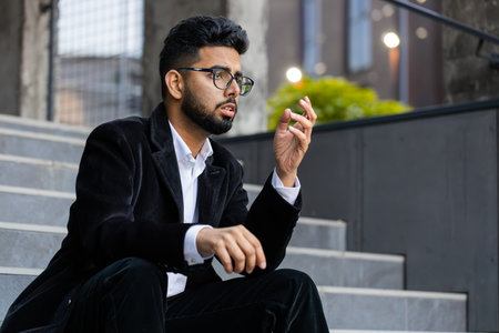 Unhappy sad Indian business man frustrated stress pensive feeling bad after company unemployment lost job problem solution crisis outdoor. Arabian Hindu freelancer guy sitting on stairs downtown cityの写真素材