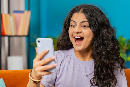 Happy woman use mobile smartphone typing browsing say Wow yes, celebrating success victory, winning lottery jackpot goal achievement play game good positive news, triumph. Girl at home in room on sofaの写真素材