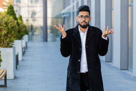 What. Why. Surprised frustrated Indian businessman raising hands asking reason of failure, demonstrating disbelief irritation by troubles outdoors. Confused Arabian Hindu freelancer guy in city streetの写真素材