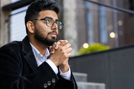 Indian businessman clasping hands wishing luck praying to God asking blessing help forgiveness wish luck outdoor. Arabian Hindu freelancer guy in downtown city street. Business people lifestyleの写真素材