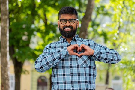 I love you. Indian young man makes symbol of love, showing heart sign to camera express romantic feelings, express sincere positive feelings outdoors. Charity, gratitude, donation. on city streetの写真素材