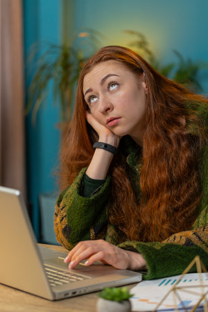 Bored sleepy businesswoman worker working on laptop computer yawns, leaning on hand at home office desk. Exhausted tired woman freelancer workaholic lady. Employment, occupation, workless. Verticalの写真素材