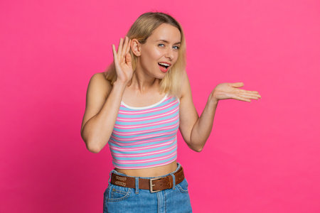 I cant hear you. What. Caucasian woman trying hear you looking confused and frowning keeping arm near ear for louder voice asking to repeat, to hear information deafness. Young girl on pink backgroundの写真素材