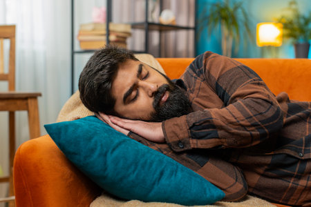 Tired Indian Hindu man lying down in bed taking a rest. Carefree peaceful guy napping, falling...