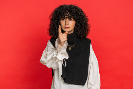 Quarrel. Displeased aggressive unhappy Caucasian young woman with curly hair gesturing hands with irritation and displeasure, blaming scolding for failure, asking why this happened on red backgroundの写真素材