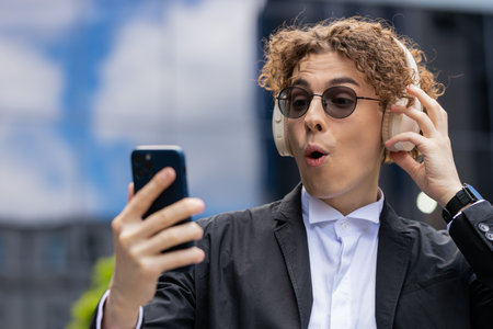 Happy relaxed young Caucasian businessman in wireless headphones dancing, listening favorite...