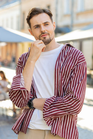 Sad unhappy bearded man thinks over life concerns, suffers from unfair situation. Problem, feeling bad annoyed, burnout grief. Frustrated depressed lonely young guy standing in city street. Verticalの写真素材