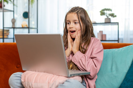 Surprised happy girl child using laptop computer, receive good news message, shocked by sudden victory celebrate lottery game jackpot win purchases online shopping at home. Lifestyle technologies.の写真素材