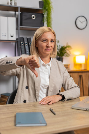 Dislike. Upset mature businesswoman working on laptop at home office showing thumbs down sign gesture, expressing discontent, disapproval, dissatisfied bad work. Displeased serious female freelancer.の写真素材