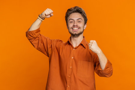 Happy joyful Caucasian man celebrating success victory, winning birthday, lottery jackpot goal achievement play game good positive news triumph. Young adult guy isolated on orange studio backgroundの写真素材