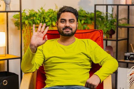 Indian man smiling friendly at camera and waving hands gesturing hello hi, greeting or goodbye...