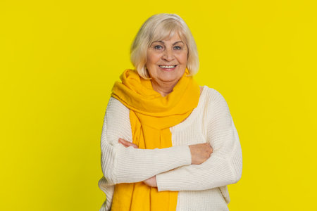 Portrait of happy senior old woman smiling friendly, glad expression looking at camera dreaming, resting relaxation feel satisfied good news. Elderly grandmother pensioner on yellow background indoorsの写真素材