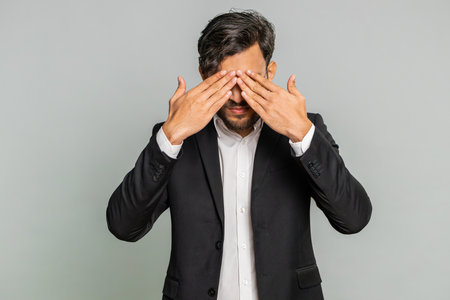 Dont want to look at this, awful. Afraid shocked Indian businessman closing eyes with hand showing stop gesture, confused shy scared reject to watch. Male Arabian man guy isolated on gray backgroundの写真素材