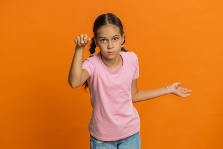 Knock-knock who is there. Confused excited young preteen child girl kid knocking door gesture asking who is at home, feeling embarrassed, no idea, being clueless and uncertain on orange backgroundの写真素材