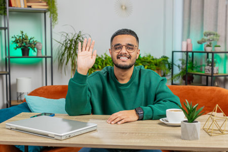 Indian smiling man smiling friendly at camera and waving hands gesturing hello hi, greeting or...