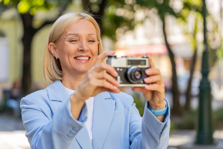 Smiling happy excited mature Caucasian businesswoman photographer in formal suit using vintage...