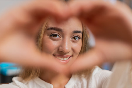 Portrait of happy Caucasian young woman at home living room couch makes symbol of love, showing heart sign to camera, express romantic feelings express sincere positive feelings. Lifestyleの写真素材