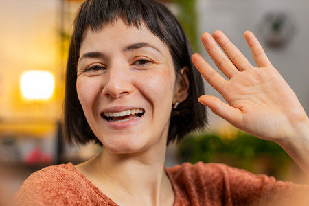 POV of young woman making online video call talking waving hand hello looking at camera blowing kiss. Communication, meeting. Smiling Hispanic girl blogger making smartphone conversation at home.の写真素材