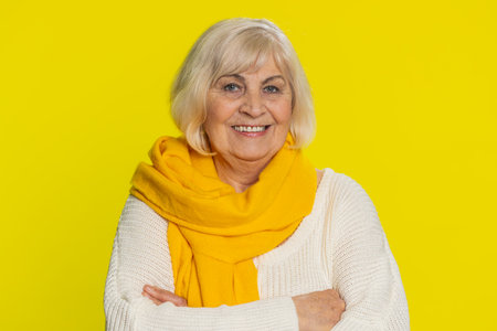 Portrait of happy senior old woman smiling friendly, glad expression looking at camera dreaming, resting relaxation feel satisfied good news. Mature grandmother pensioner on yellow background indoorsの写真素材