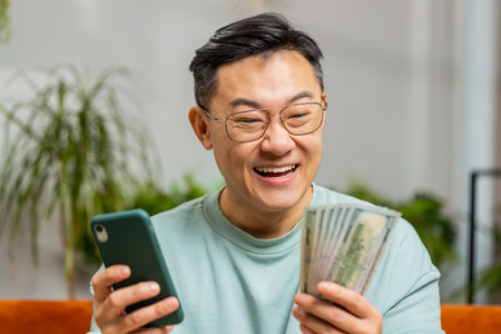 Rich happy Asian man planning budget use smartphone calculator app count money cash calculate...