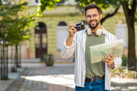 Caucasian young man tourist traveling on weekends exploring town looking city map, making photo pictures on retro vintage camera outdoors. Happy adult guy traveler on urban city street. Lifestyles.の写真素材