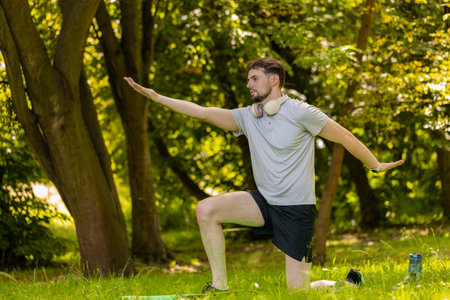 Athletic sporty fit man doing workout yoga breathing exercise on sports mat in park. Raising hands....