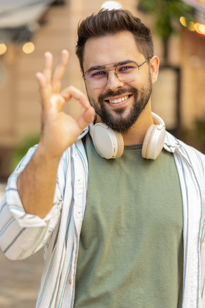 Portrait of smiling young millennial guy looking at camera showing hand ok sign. Caucasian handsome man showing everything fine success gesture body language. Tourist in glasses smiling at camera.の写真素材
