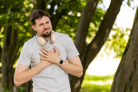 Young adult sports man runner jogger having heart attack or chest pain after running workout in...