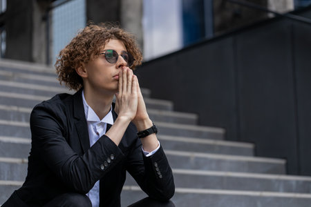Pensive businessman in suit with hands joined making company decision. Corporate leader pondering in downtown.の写真素材