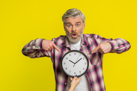 Mature man lifts clock with worried face highlighting close call and racing anxiety. Guy conveys overwhelming deadline rush signaling imminent lateness, worrying to be punctual, stressの写真素材