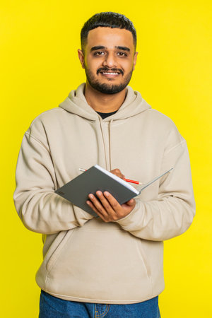 Thoughtful journalist young man making notes, writing down thoughts with pen into notepad notebook diary, to do list, good idea inspiration. Guy isolated on yellow background. Verticalの写真素材