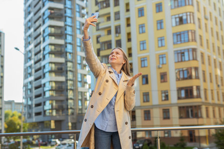 Mature businesswoman trying to catch a communication signal and Internet on mobile phone, raised the phone up for better connection in downtown city street. Frustrated girl in city town.の写真素材