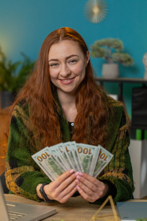 Happy business woman counting money cash and using laptop at home desk. Successful freelancer girl getting bundle of money in office calculates dividends cash earnings profits and finances. Verticalの写真素材
