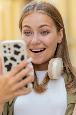 Excited happy joyful winner young woman using smartphone looking at screen browsing celebrating win good message news. Teenage girl traveler with mobile phone in urban street outdoors.の写真素材