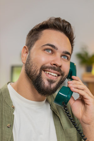 Closeup of smiling young man making wired telephone call conversation with friends sitting on couch at home. Happy excited guy male enjoying old-fashioned retro phone from 90s talking in living room.の写真素材