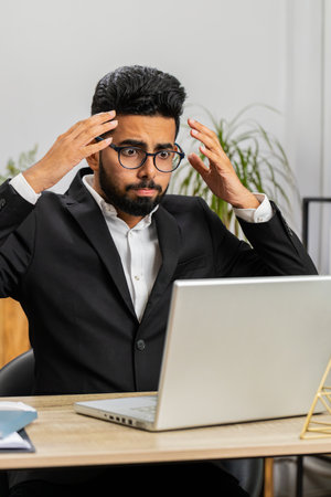 Unhappy Indian businessman programmer software developer working on laptop loses becoming surprised...