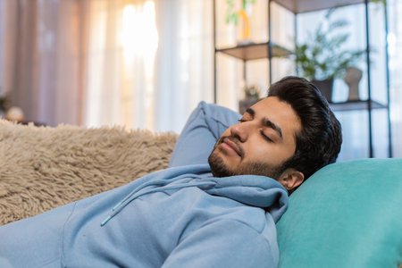 Tired man lying down on comfortable couch, taking rest, daytime nap. Carefree guy relaxing, falling asleep at home. Adult male resting with eyes closed, looking calm and serene.の写真素材