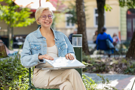 European woman in city street closes laptop screen finishing working online distant job browsing website chatting, looking at camera. Girl use notebook, sends messages, watching movies.の写真素材