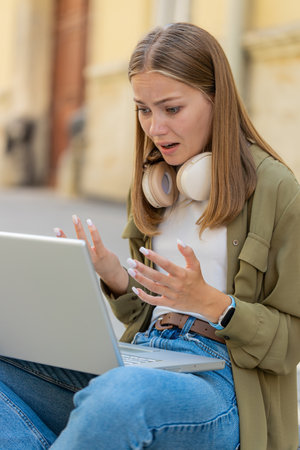 Displeased Caucasian woman using laptop typing browsing working, loses becoming surprised sudden lottery results bad news fortune loss game fail computer virus. Girl female sitting on street city.の写真素材