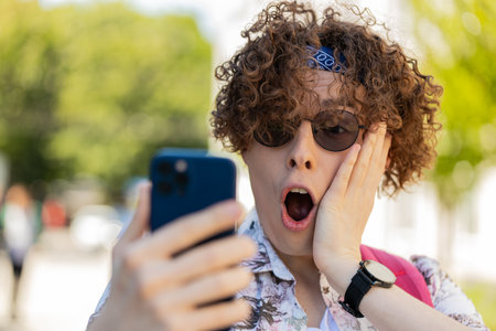 Young man using mobile smartphone celebrating win good message news, lottery jackpot victory, giveaway online outdoors. Wow emotion. Happy guy tourist standing in urban city street. Town lifestylesの写真素材