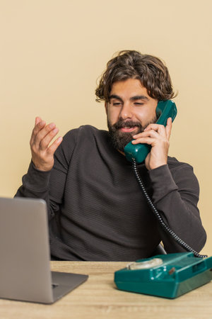 Happy bearded businessman sitting at table talking on wired telephone call conversation...