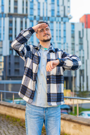 Serious sad businessman standing outside office looking around waiting for business meeting impatient man, dissatisfied looks at wristwatch checks time on watch annoyed by being late lateness concept.の写真素材