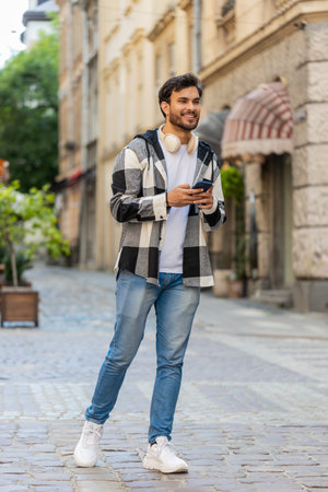 Tourist traveler young man using smartphone typing text messages looking for a way on map in mobile navigator app outdoors. Guy male walking passes by urban city street background.の写真素材