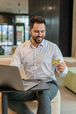 Smiling Caucasian businessman using bank credit card and laptop for online shopping payments in...