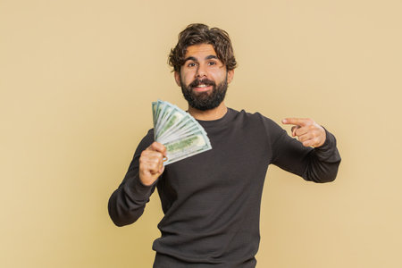 Pleased boss young man waving money dollar cash banknotes bills like a fan, success business career, lottery winner, big income, wealth. Adult guy isolated on beige background.の写真素材