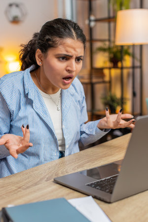 Nervous woman quarrelling laptop call online at home office desk. Emotional Indian girl talking aggressively computer video call. Stressed lady scolding subordinates and closing laptop. Vertical.の写真素材