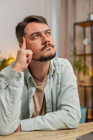 Smart focused man freelancer guy pensive thoughtful sitting at table home office sitting with laptop thinks about solving problem with online service app makes decision deep in thoughts. Verticalの写真素材